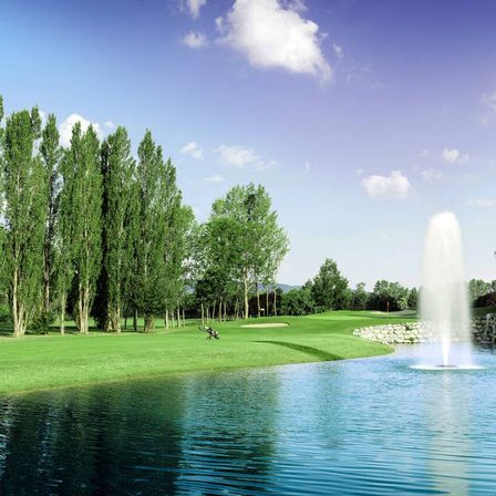 Ein Golfplatz mit einem Brunnen in der Mitte eines Sees, umgeben von Bäumen und einem klaren blauen Himmel.
