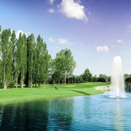 Ein Golfplatz mit einem Brunnen in der Mitte eines Sees, umgeben von Bäumen und einem klaren blauen Himmel.