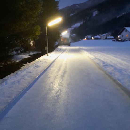 Eine verschneite Straße mit Straßenlaternen und einem Berg im Hintergrund bei Nacht.