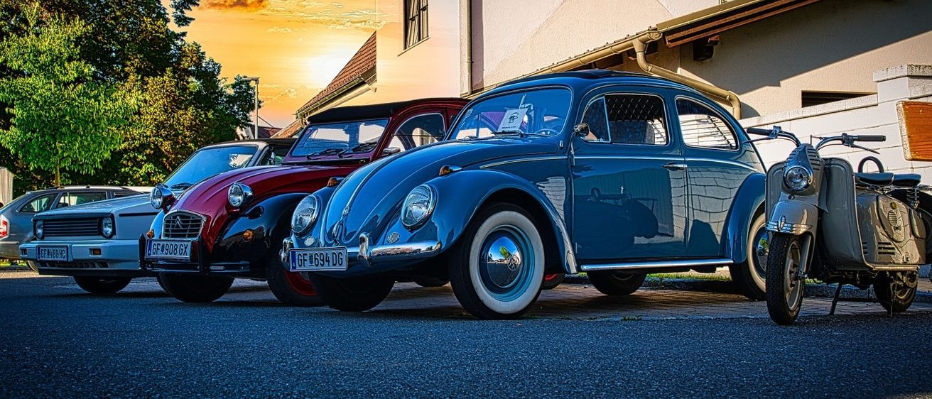 Drei Oldtimer parken vor einem Haus, mit einem wunderschönen Sonnenuntergang im Hintergrund.
