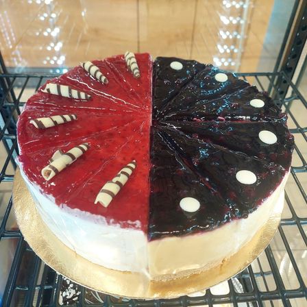Ein Käsekuchen mit roten und schwarzen Toppings auf einem goldenen Teller, ausgestellt auf einem schwarzen Regal.