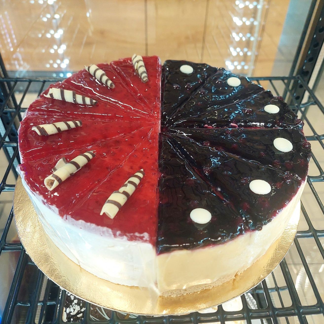 Ein Käsekuchen mit roten und schwarzen Toppings auf einem goldenen Teller, ausgestellt auf einem schwarzen Regal.