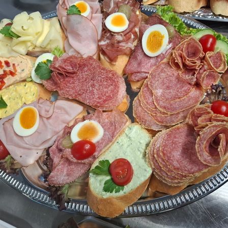 Eine silberne Platte mit einer Auswahl an Fleisch, Käse und Gemüse. Beinhaltet Scheiben von Salami, Schinken und Eiern.