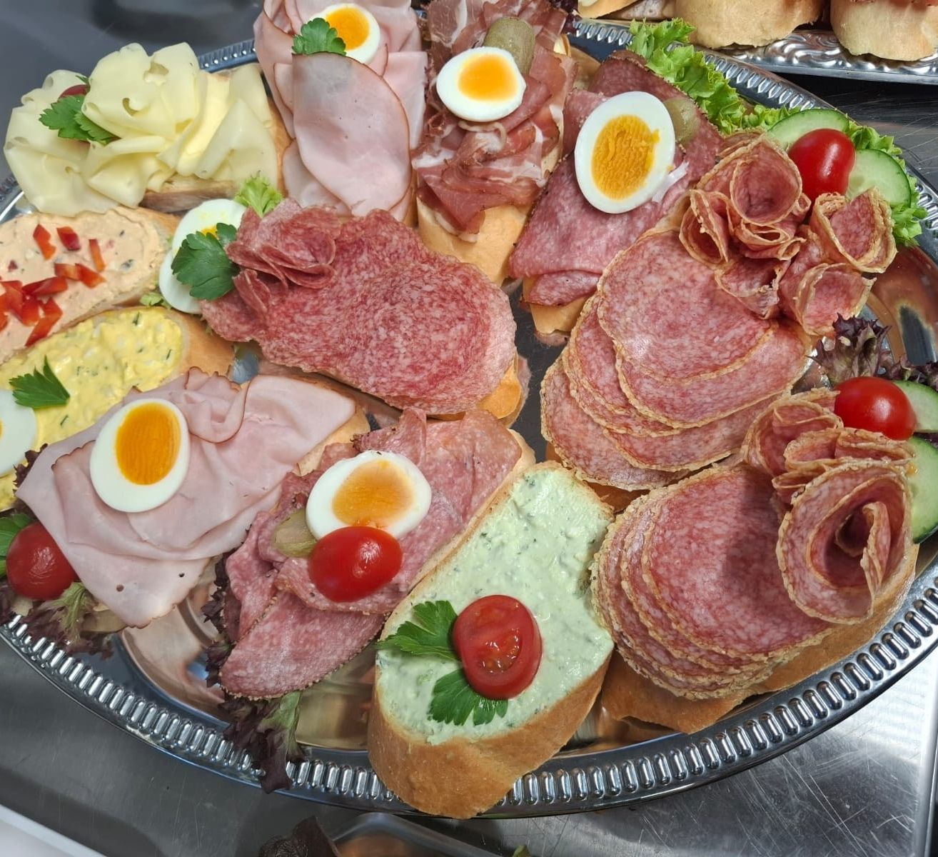 Eine silberne Platte mit einer Auswahl an Fleisch, Käse und Gemüse. Beinhaltet Scheiben von Salami, Schinken und Eiern.