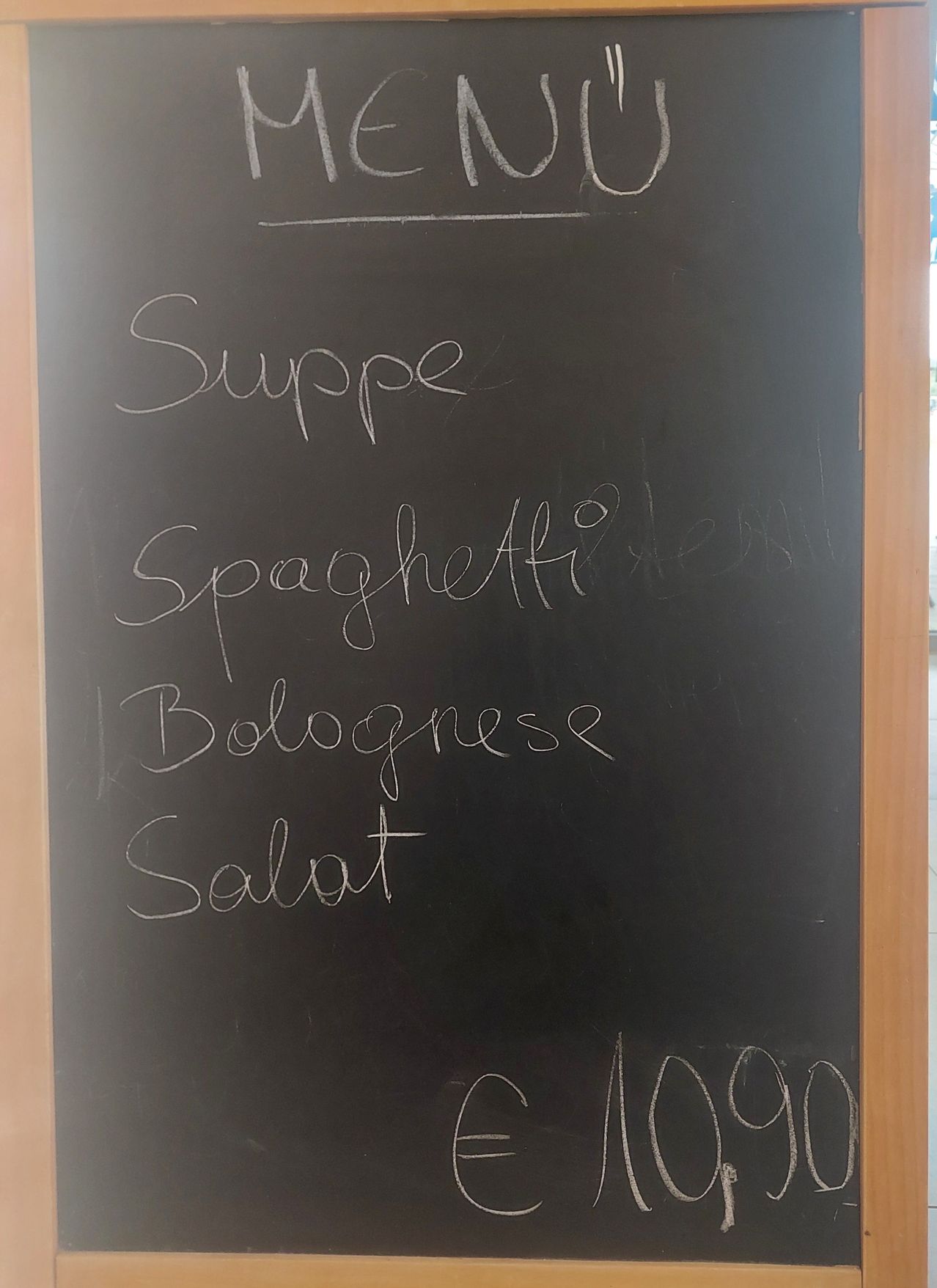 Ein Kreidetafel mit einem in kursiver Schrift geschriebenen Menü. Es bietet vier Gerichte an: Suppe, Spaghetti Bolognese und Salat. Jedes Gericht kostet 10,00.