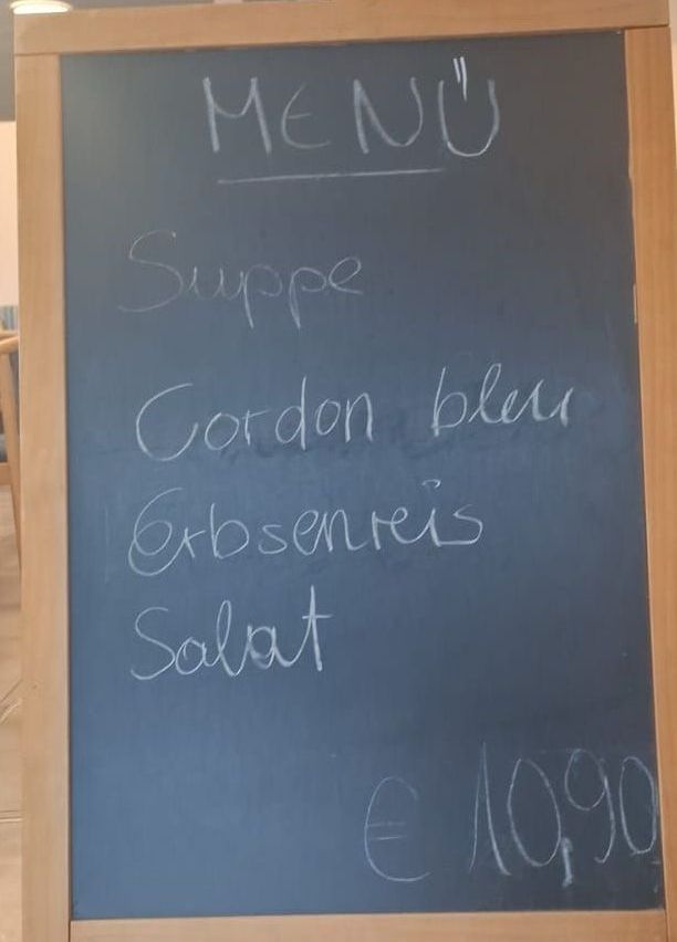 Ein Kreidetafel-Menü mit einem Holzrahmen. Es listet vier Gerichte auf: 'Suppe', 'Gordon bleu', 'Erbseneis' und 'Salat'. Der Preis ist mit 10,90 Euro angegeben.