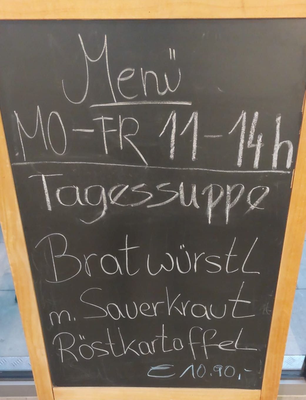Ein Kreidetafel-Menü listet tägliche Suppe, Bratwurst mit Sauerkraut und Röstkartoffeln auf, verfügbar von Montag bis Freitag von 11 bis 14 Uhr.