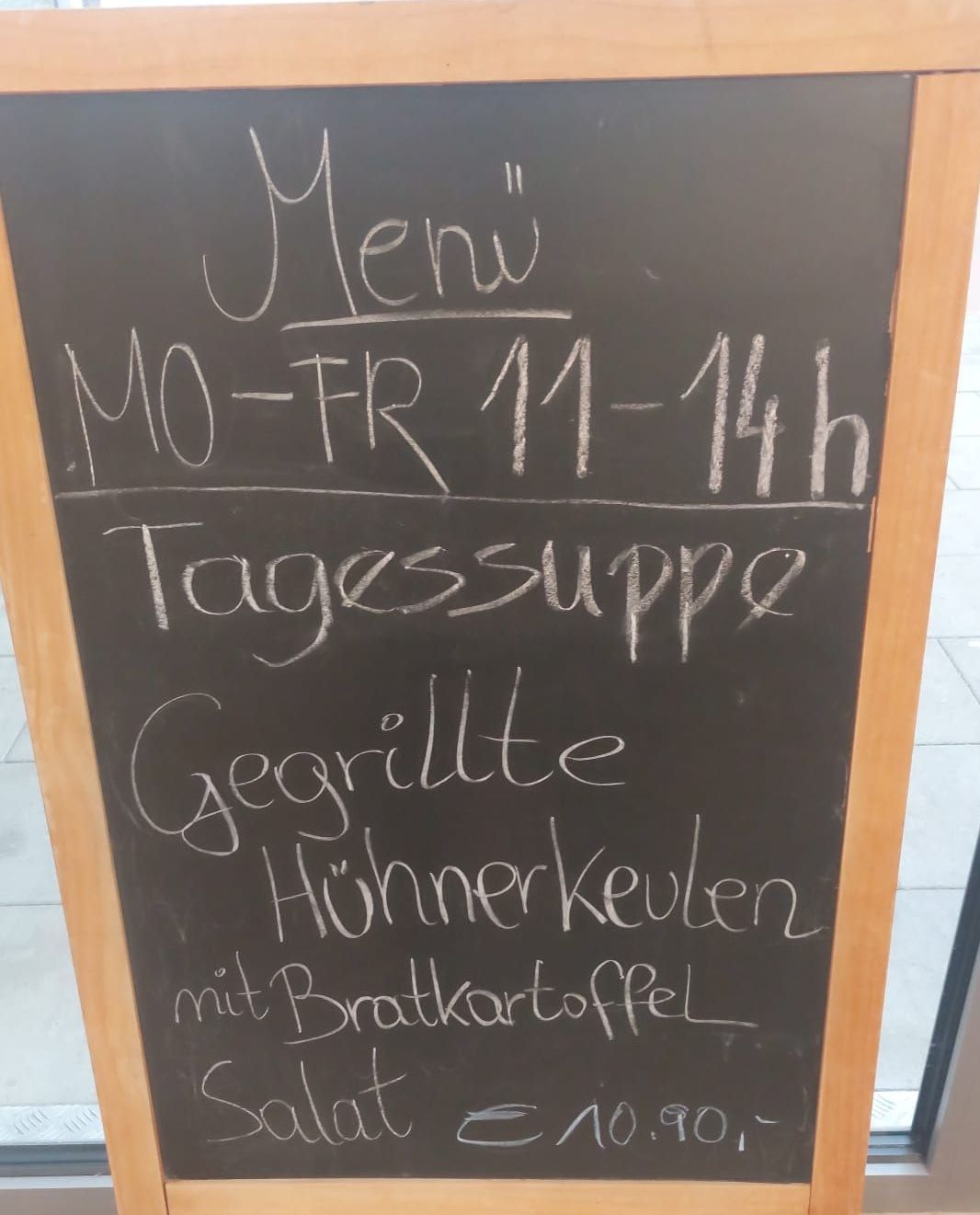 Ein Tafelmenü-Schild zeigt ein Tagesmenü mit gegrillten Hähnchenkeulen und Bratkartoffeln von Montag bis Freitag, 11 bis 14 Uhr an.