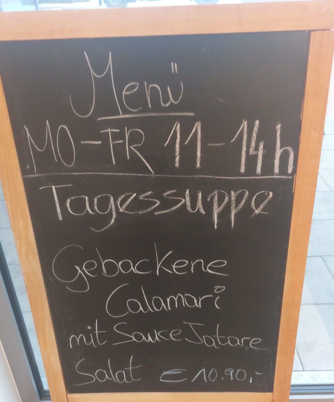 Ein Kreidetafelmenü in einem Restaurant. Es ist von Montag bis Freitag von 11 Uhr bis 14 Uhr geöffnet. Es gibt gebackenes Huhn, Calamari mit Sauce und ein Dessert auf der Speisekarte.