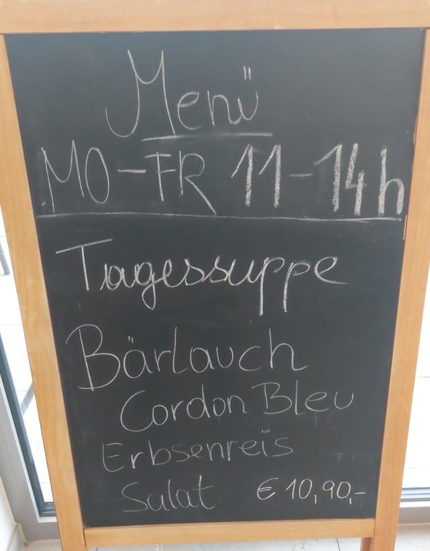 A chalkboard menu with offerings for Monday to Friday from 11 AM to 2 PM. Includes daily soup, Barlauch Cordon Bleu, and Erbsenreis at 10.90 Euros.