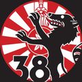 Ein kreisförmiges Emblem mit einem schwarzen Wolf, der den Mund öffnet und Zähne zeigt, der Nummer 38 und einem roten Hintergrund mit weißen Radiallinien.