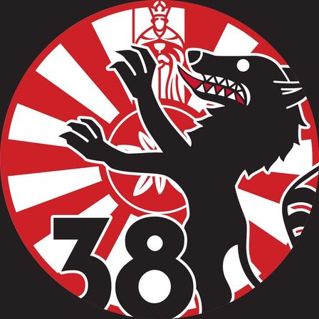 Ein kreisförmiges Emblem mit einem schwarzen Wolf, der den Mund öffnet und Zähne zeigt, der Nummer 38 und einem roten Hintergrund mit weißen Radiallinien.