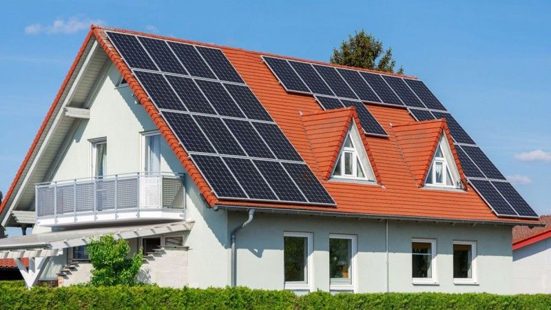 Ein modernes Haus mit einem roten Dach und Solarpanelen darauf installiert.