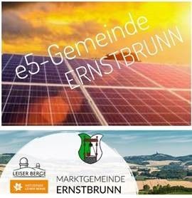 Ein Poster zeigt Solarpanele mit einem Sonnenuntergang im Hintergrund und den Worten 'e5-Gemeinde Ernstbrunn' in weißen Buchstaben. Darunter ist das Logo einer Gemeinde mit einem Gebäude und dem Text 'Marktgemeinde Ernstbrunn' zu sehen.