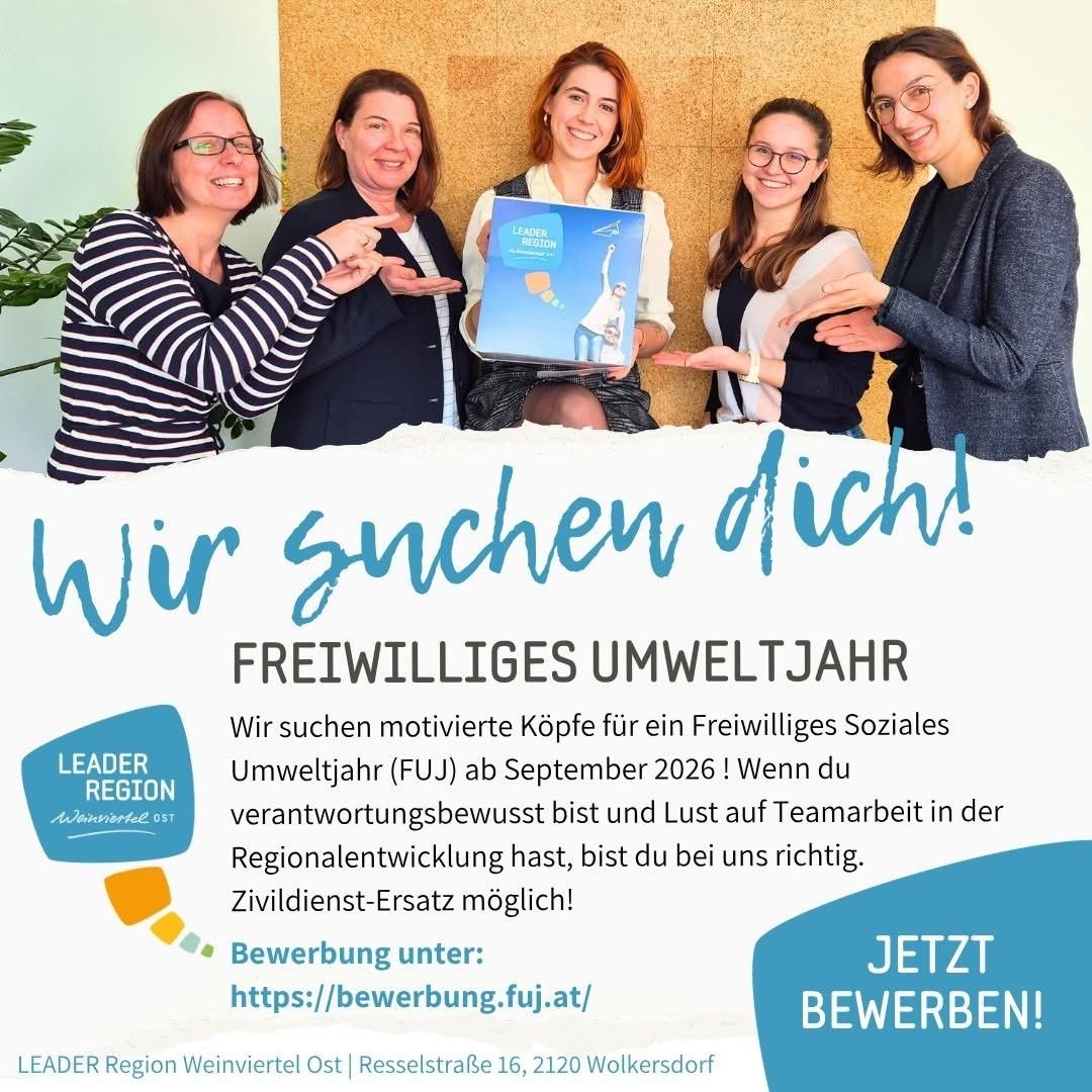 Fünf Frauen lächeln und posieren für ein Foto. Eine hält eine blaue Mappe. Auf der Mappe steht 'LEADER REGION'. Es gibt eine Einladung für Freiwillige für ein freiwilliges soziales Umweltjahr.