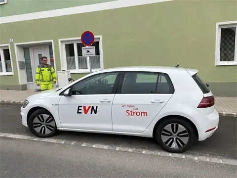 Ein weißer Elektrowagen mit den Worten EVN Strom an der Seite ist auf der Straße geparkt. Ein Mann in einem gelben Sicherheitsjacket steht in der Nähe.