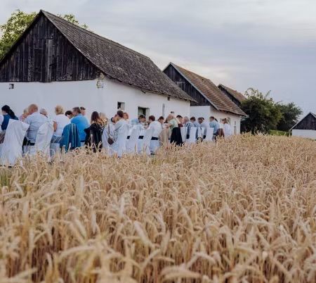 Eine Gruppe von Menschen sitzt in einem Weizenfeld für eine Zusammenkunft. Ein Scheune ist im Hintergrund.