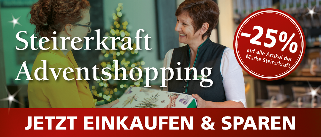 Eine lächelnde Frau mit kurzen Haaren hält ein Geschenk in der Hand, während eine weitere Person mit Brille im Hintergrund zu sehen ist. Das Bild ist vor einem Weihnachtsbaum und festlicher Dekoration angesiedelt.