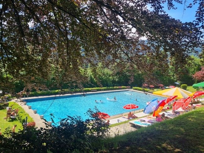 Ein sonniger Tag an einem Freibad mit Schwimmern und Leuten, die sich unter bunten Sonnenschirmen entspannen.