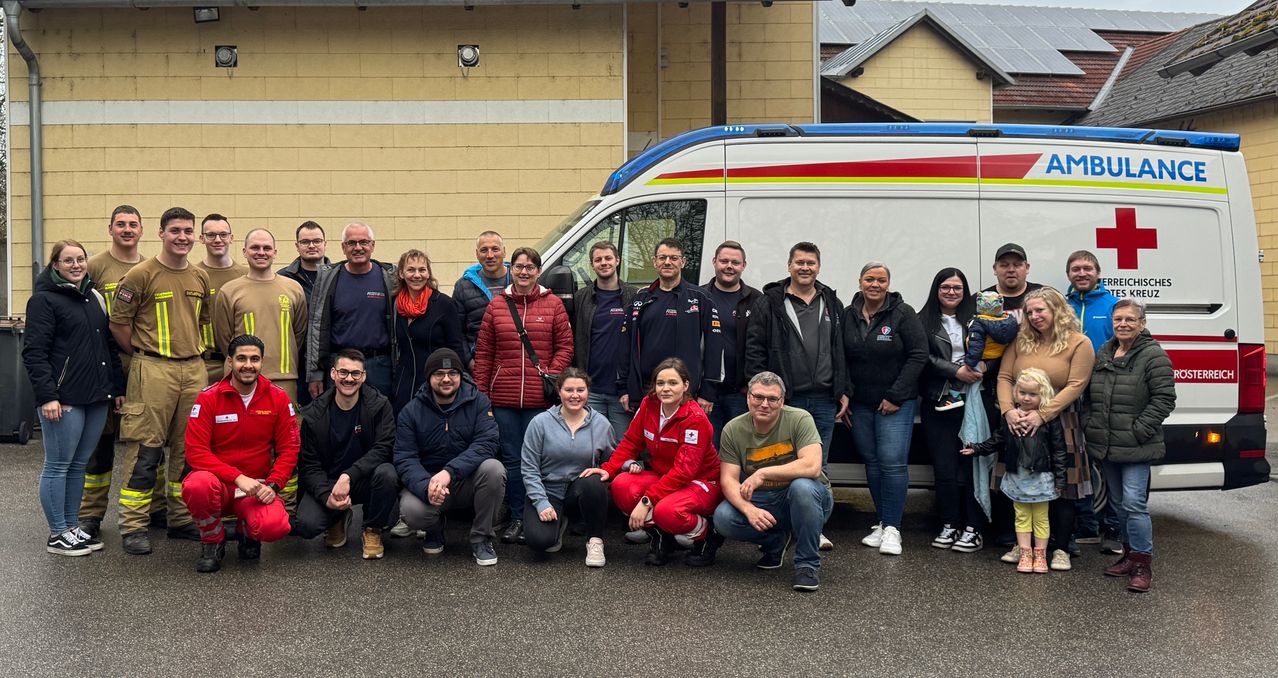 A group of people in jackets pose for a photo in front of a white ambulance with red and blue stripes.