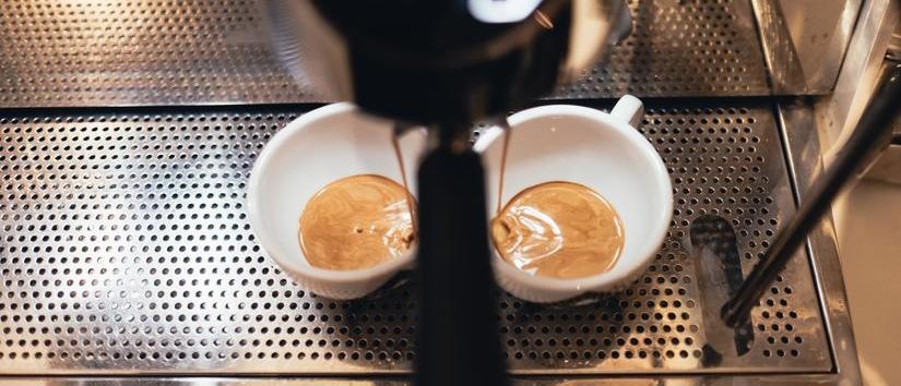 Espresso wird in zwei weiße Tassen auf dem Metalltablett einer Kaffeemaschine gegossen.