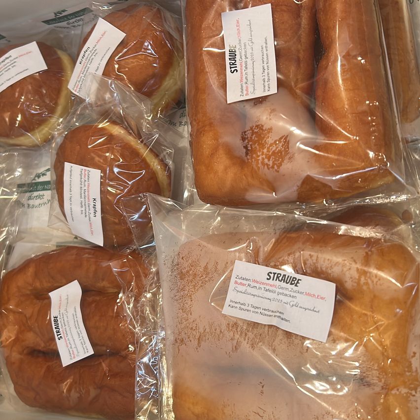 Mehrere Gebäckstücke, möglicherweise Struebe, sind in Plastiktüten verpackt. Einige sind in einzelnen Tüten und einige in einer einzigen größeren Tüte. Sie sind braun mit etwas Puderzucker darauf.