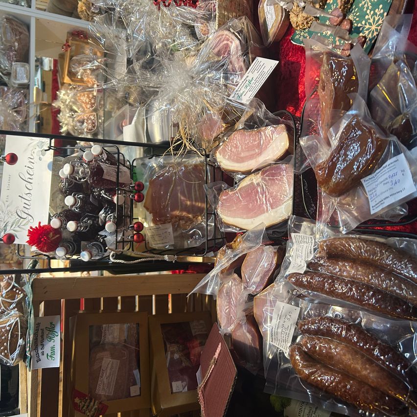 Eine Ausstellung verschiedener Fleischsorten, einschließlich Speck und Würsten, verpackt und bereit zum Verkauf in einer festlichen Umgebung.