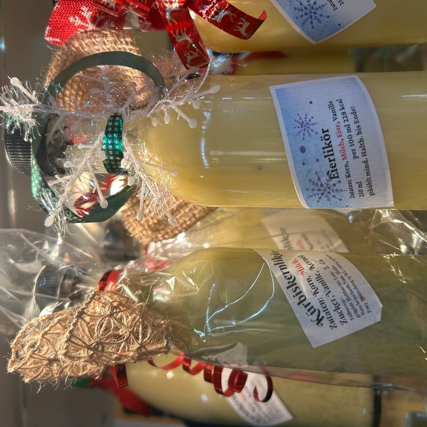 Mehrere Flaschen Eerdikor und Apricotkermilik sind in festlichen Dekorationen und Plastik eingewickelt. Jede Flasche hat ein Etikett mit Informationen zu ihren Zutaten und Nährwertangaben.