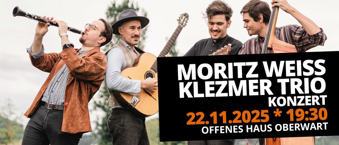 Vier Männer in traditioneller Kleidung stehen draußen mit Gitarren. Einer spielt Gitarre, ein anderer trinkt und zwei lächeln. Das Datum 22.11.2022 und das Wort MORITZ sind auf einem schwarzen Schild zu sehen.