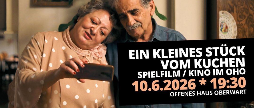 An elderly couple is taking a selfie on a sunny day. The woman holds a phone, and the man has a mustache. The background features a plant.
