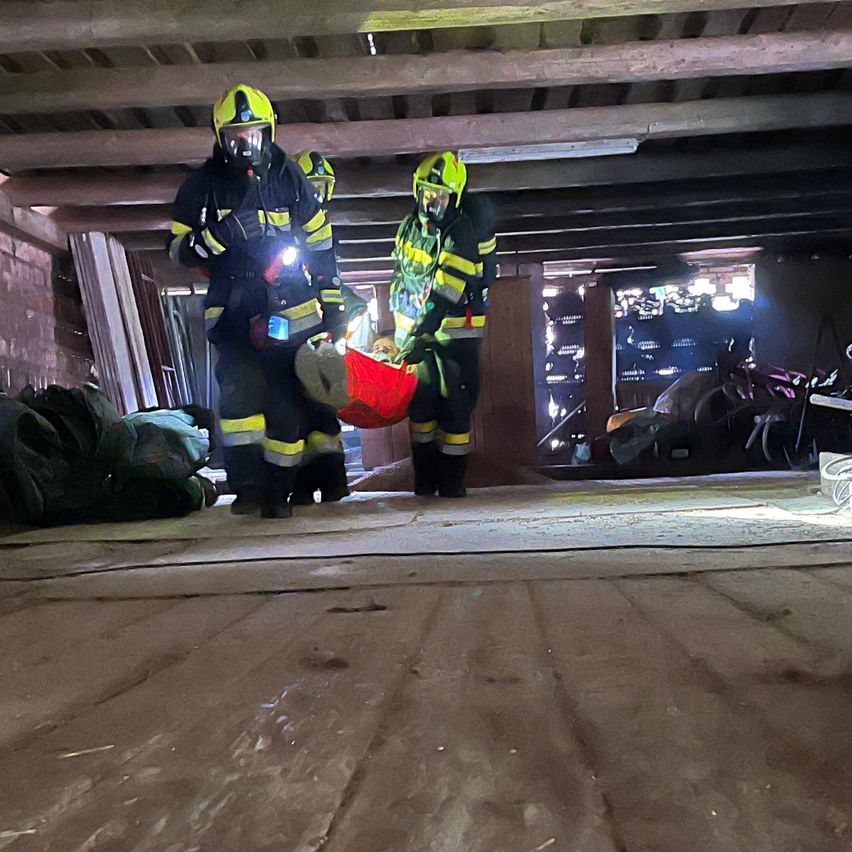 Three firefighters wearing yellow and black uniforms and helmets are carrying a person on a stretcher in a tunnel.