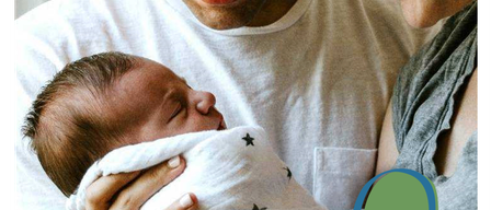 A couple with a newborn baby, both parents smiling and holding the baby in their arms. The baby is wrapped in a white blanket with stars.
