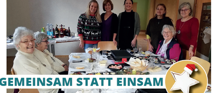 Eine Gruppe von Frauen steht lächelnd um einen festlich gedeckten Tisch herum. Der Tisch ist mit verschiedenen Speisen und Getränken gefüllt. Auf der rechten Seite ist ein Weihnachtsstern zu sehen. Das Bild hat eine festliche Überlagerung mit dem Text 'Gemeinsam statt einsam'.