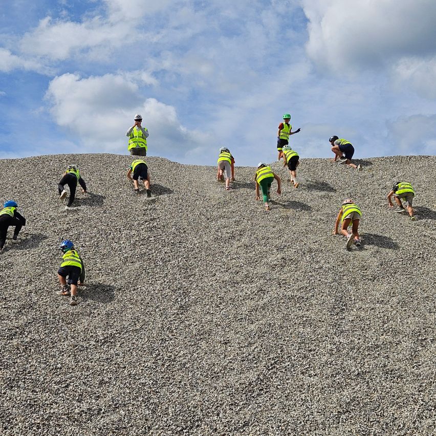 Eine Gruppe von Menschen in Sicherheitsausrüstung klettert unter einem teilweise bewölkten Himmel eine Kieshaufen.