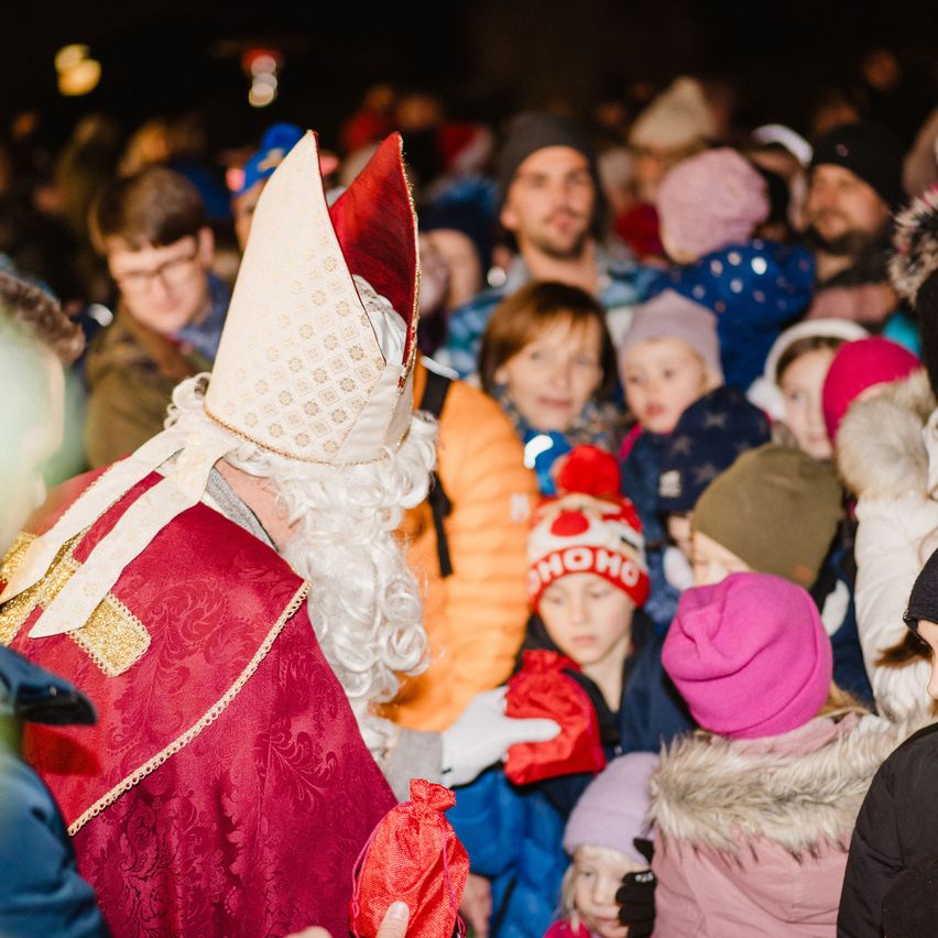 Eine Menschenmenge, darunter auch Kinder, versammelt sich um einen als Weihnachtsmann verkleideten Mann, der einen roten Beutel hält und mit der Menge interagiert.