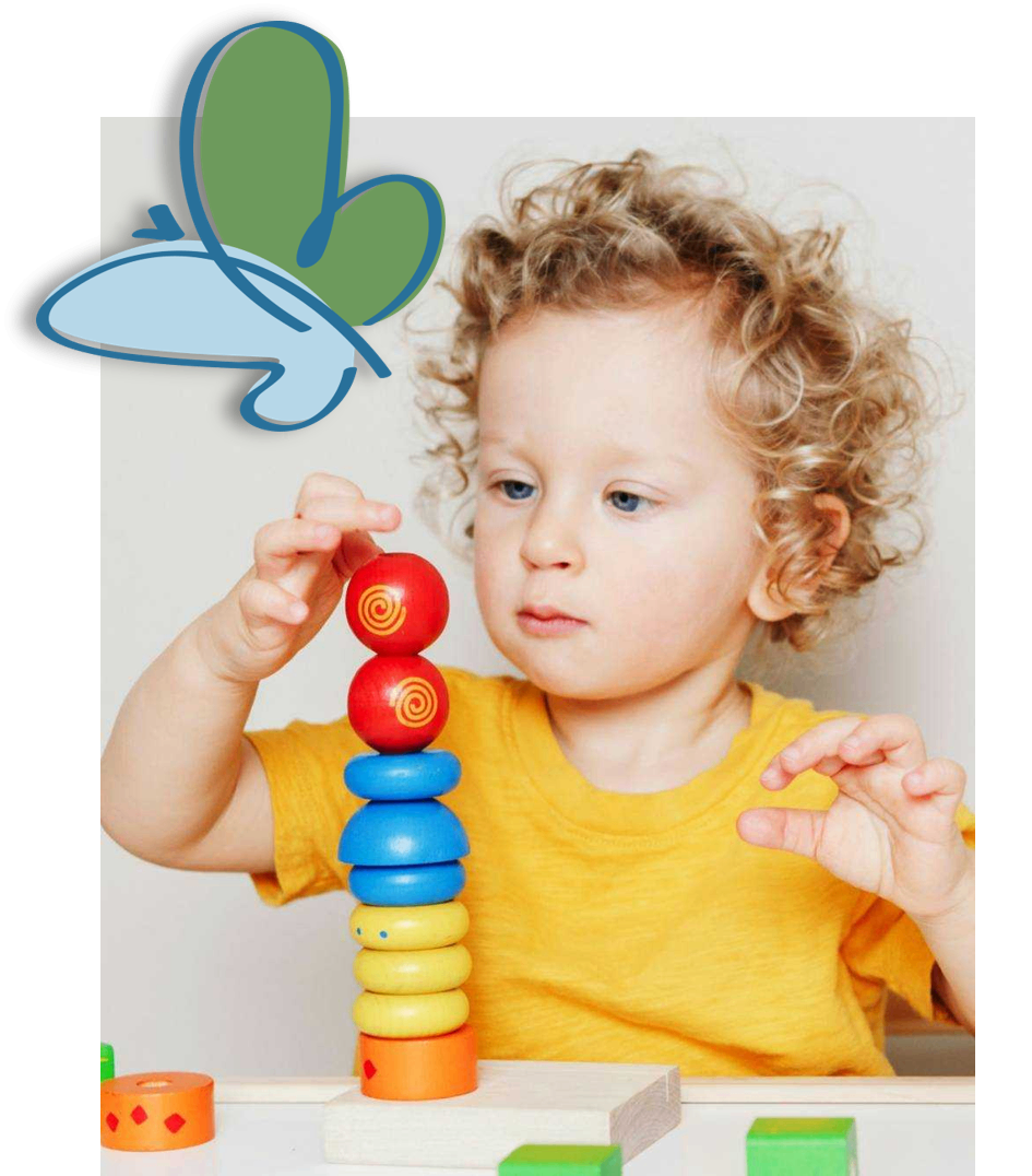 Ein kleines Kind mit lockigem Haar spielt mit einem Stapel bunter Ringe. Das Kind trägt ein gelbes T-Shirt.