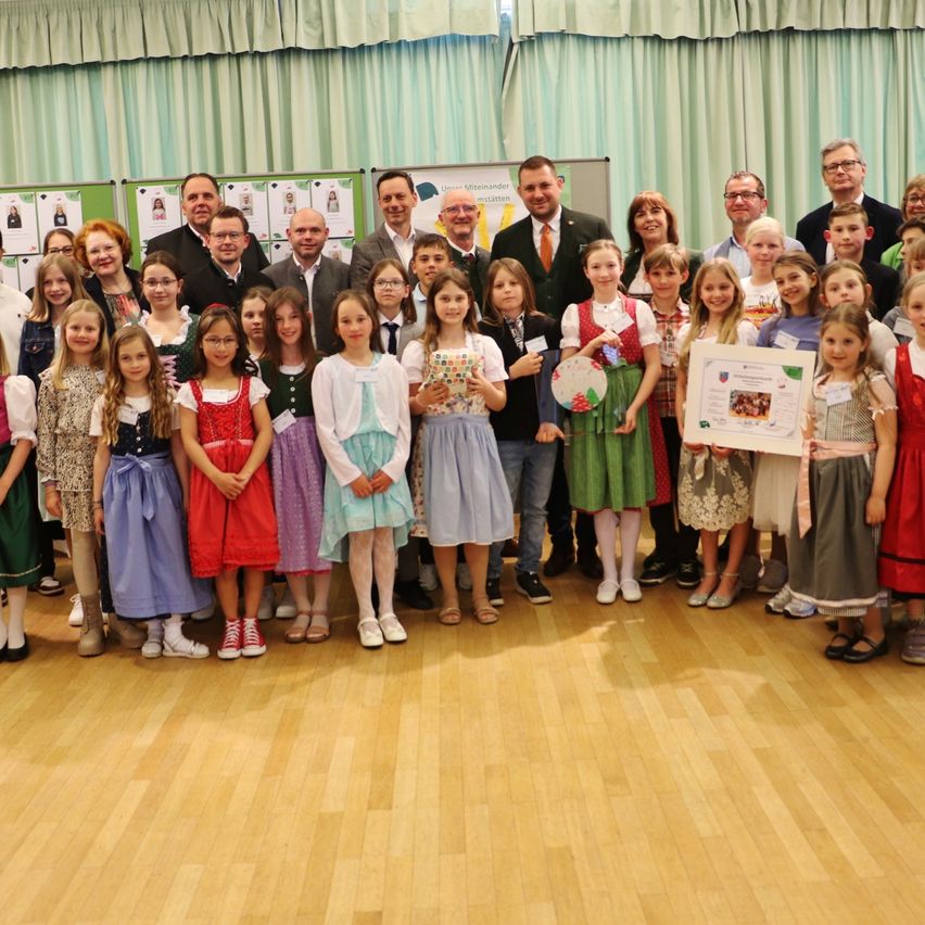 Group photo of adults and children in traditional clothing standing in a room. A woman holds a certificate.