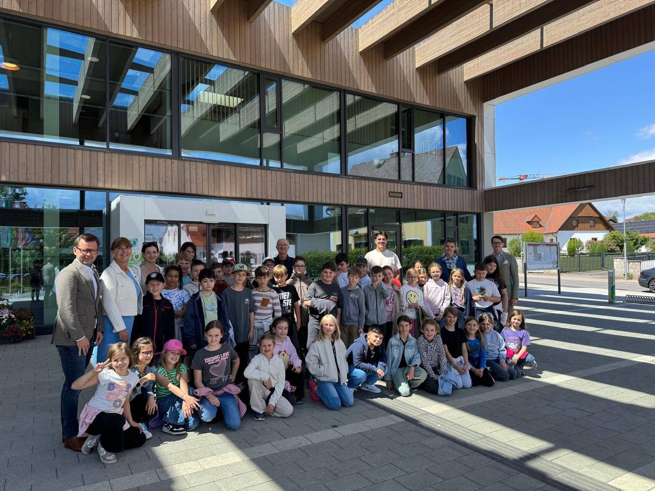 Eine Gruppe von Kindern, Erwachsenen und Lehrern posiert für ein Foto vor einem modernen Gebäude mit Glasfenstern.