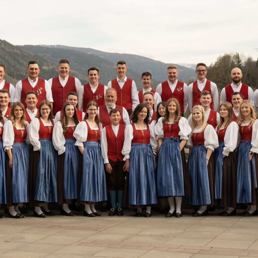 Ein Chorensemble in traditioneller deutscher Kleidung posiert für ein Foto vor einem Berg.