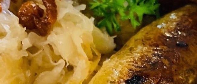 Ein Teller deutscher Küche mit gegrillten Würsten, Sauerkraut und Soße. Petersilie garniert das Gericht.