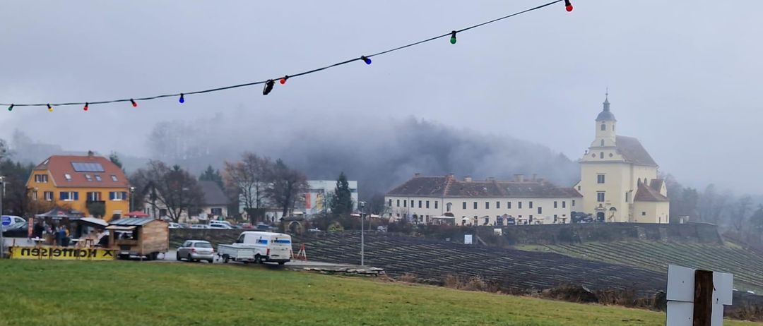 Ein nebliger Morgen mit einem großen Gebäude im Hintergrund, einem Feld, einem Pickup-Truck und einem Auto, das am Straßenrand geparkt ist, zusammen mit einer Schnur bunter Lichter.