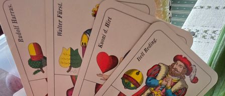 Mehrere Spielkarten mit verschiedenen Illustrationen sind mit Radieschen und einer weißen Kerze auf einem Tisch angeordnet. Jede Karte hat ein einzigartiges Design und Text.