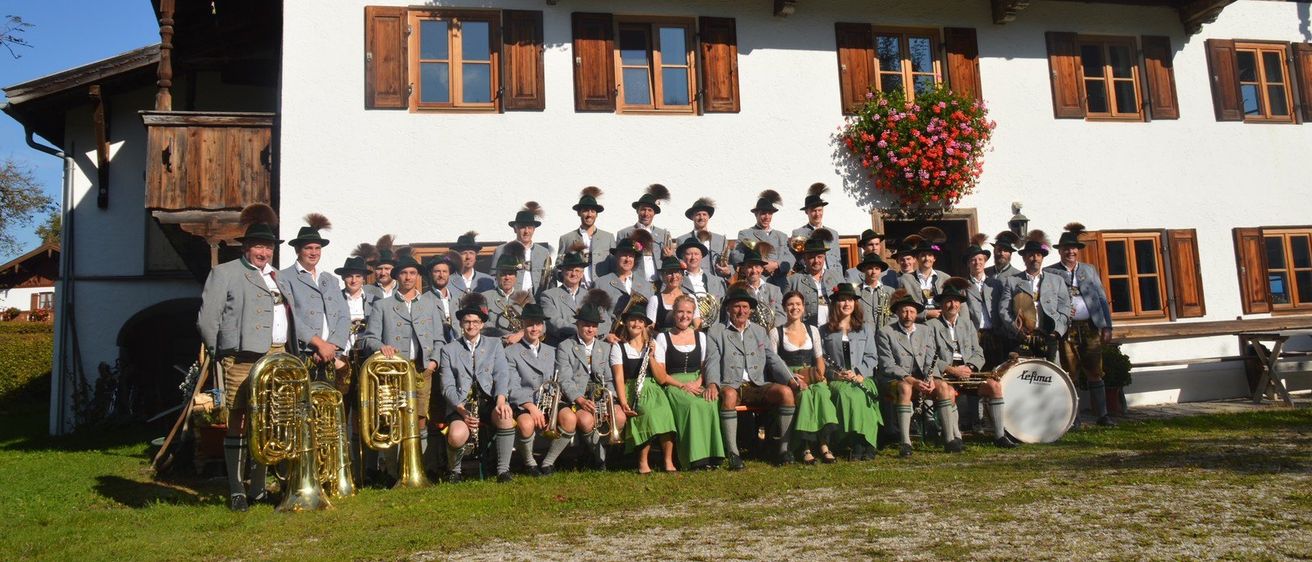 Ein Blasorchester posiert für ein Gruppenfoto vor einem Haus mit Blumenkörben auf dem Balkon.