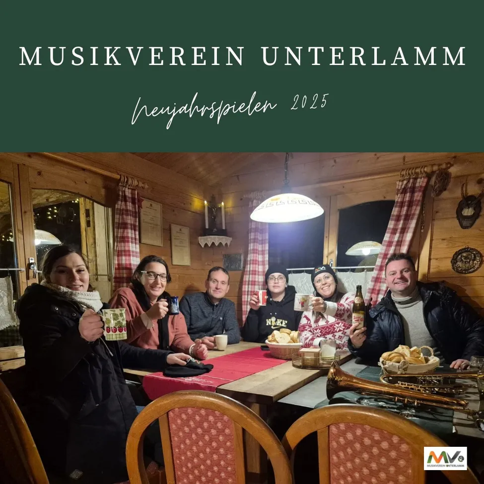 Eine Gruppe von Menschen sitzt in einer Hütte um einen Tisch herum, lächelt und hält Tassen. Sie scheinen eine Mahlzeit gemeinsam zu genießen. Der Tisch ist mit Brot, Tassen und einer Flasche gedeckt. Eine Trompete steht auf dem Tisch. Der Raum ist warm beleuchtet, eine Lampe hängt von der Decke. Das Bild hat einen Wasserzeichen in der unteren rechten Ecke.