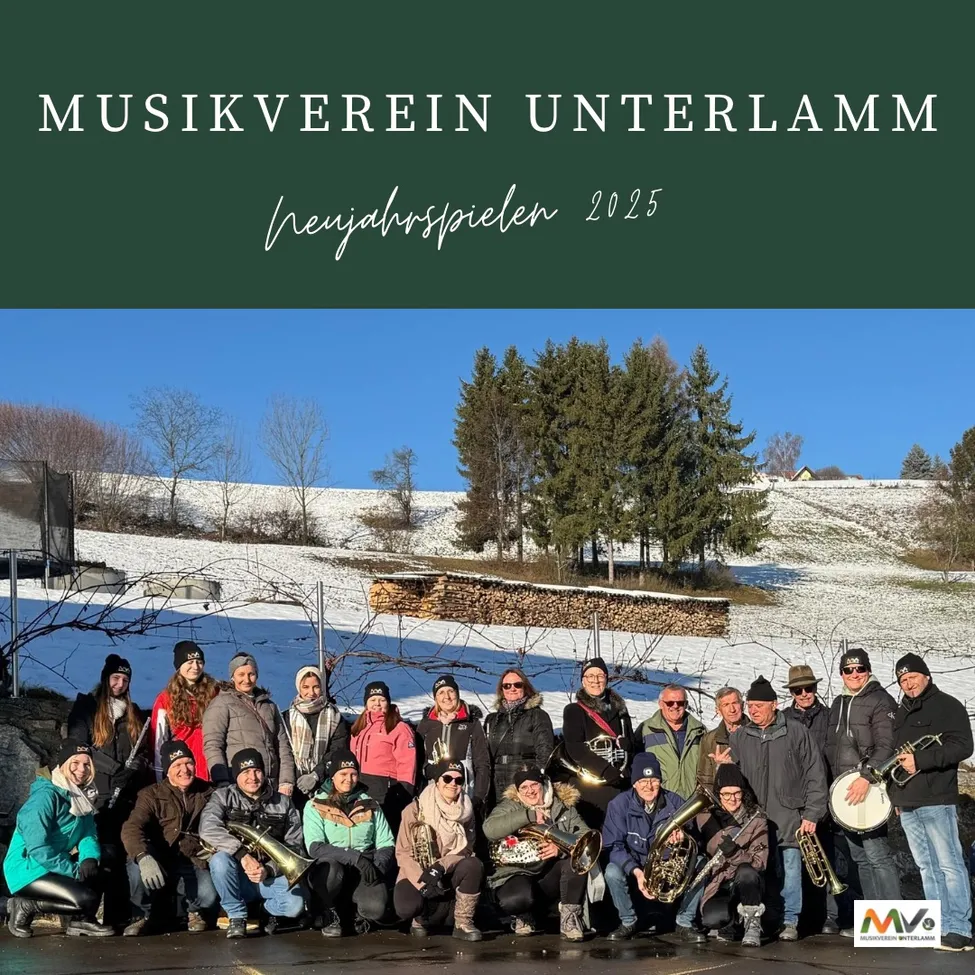 Ein Gruppenfoto des Musikverein Unterlamm aus dem Jahr 2025 mit schneebedecktem Hintergrund, Bäumen und einem Gebäude. Die Mitglieder halten verschiedene Instrumente, darunter Trompeten und Tuben.