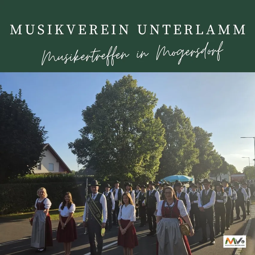 Eine Gruppe von Menschen in traditioneller Kleidung, die bei einem Umzug mit Bäumen und einem Haus im Hintergrund marschiert. Der Text lautet 'Musikverein Unterlamm Musiktreffen in Mogersdorf.'