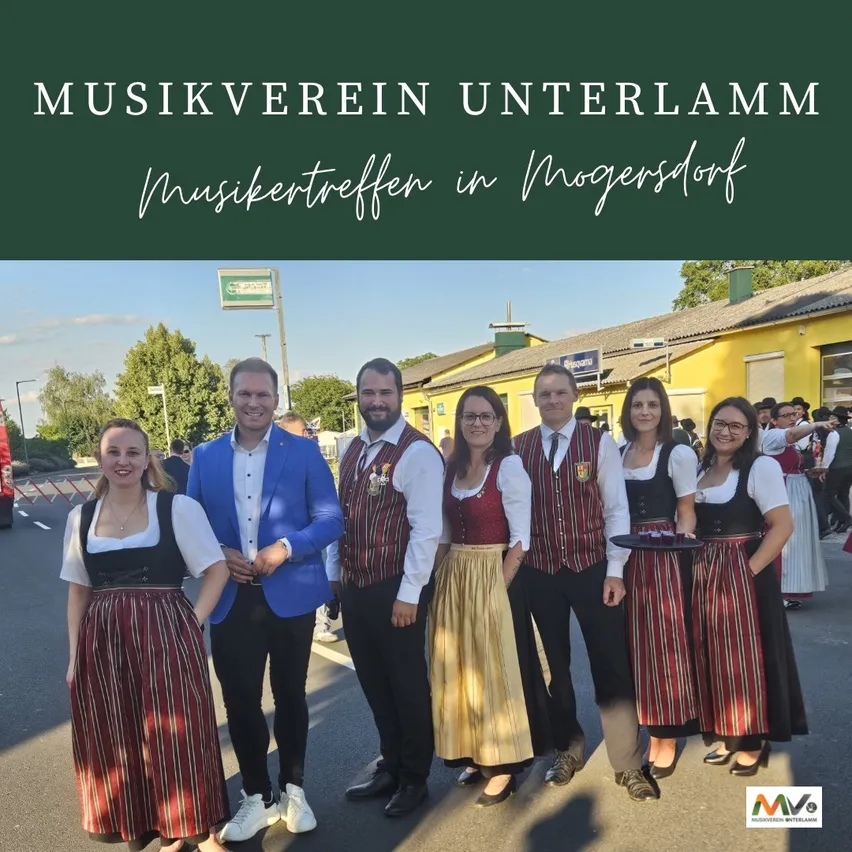Eine Gruppe von Menschen in traditioneller deutscher Kleidung steht vor einem Gebäude mit dem Schriftzug 'Musikverein Unterlamm'. Sie lächeln und posieren für ein Foto.