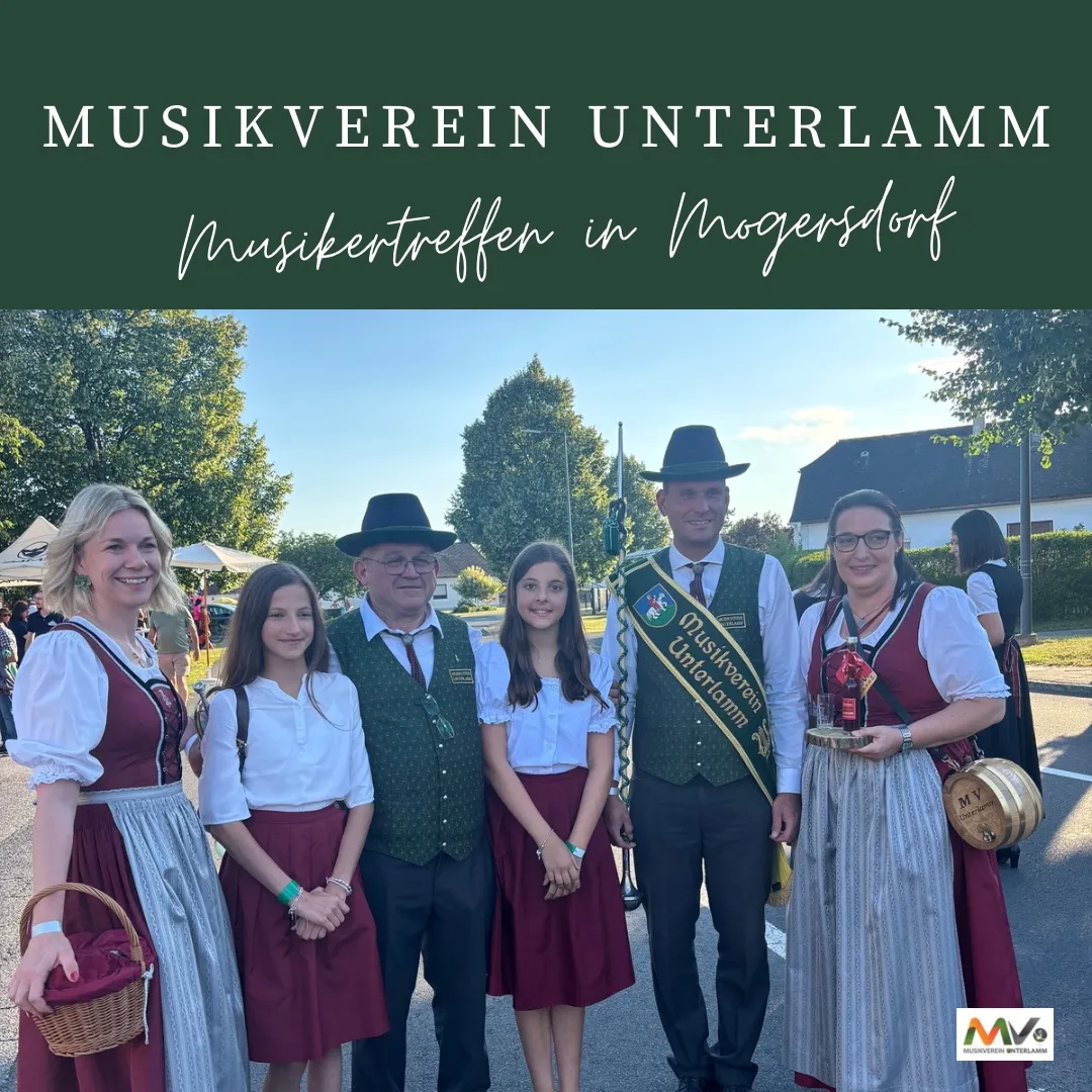 Eine Gruppe von Menschen in traditioneller deutscher Kleidung, die vor einem Gebäude mit einem Banner steht, auf dem 'Musikverein Unterlamm Musiktreffen in Mogersdorf' steht. Das Bild fängt einen Moment der Feier mit einer festlichen Atmosphäre ein.