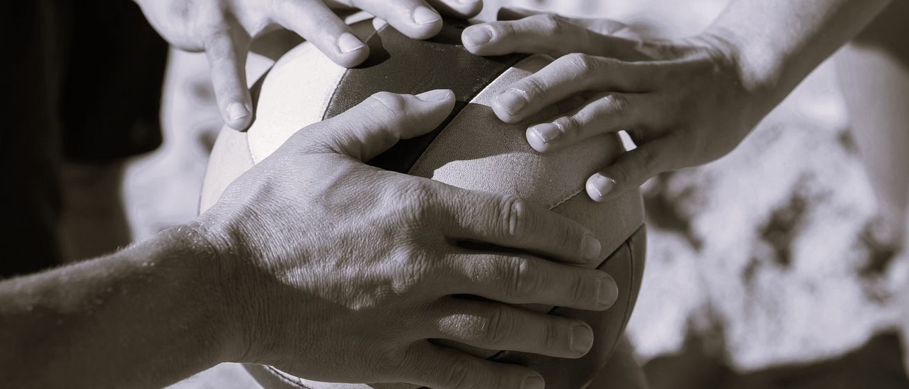 Mehrere Hände halten einen Ball, möglicherweise einen Volleyball, bei einer Teambildungsübung. Der Ball ist mit weißem und schwarzem Leder bedeckt.