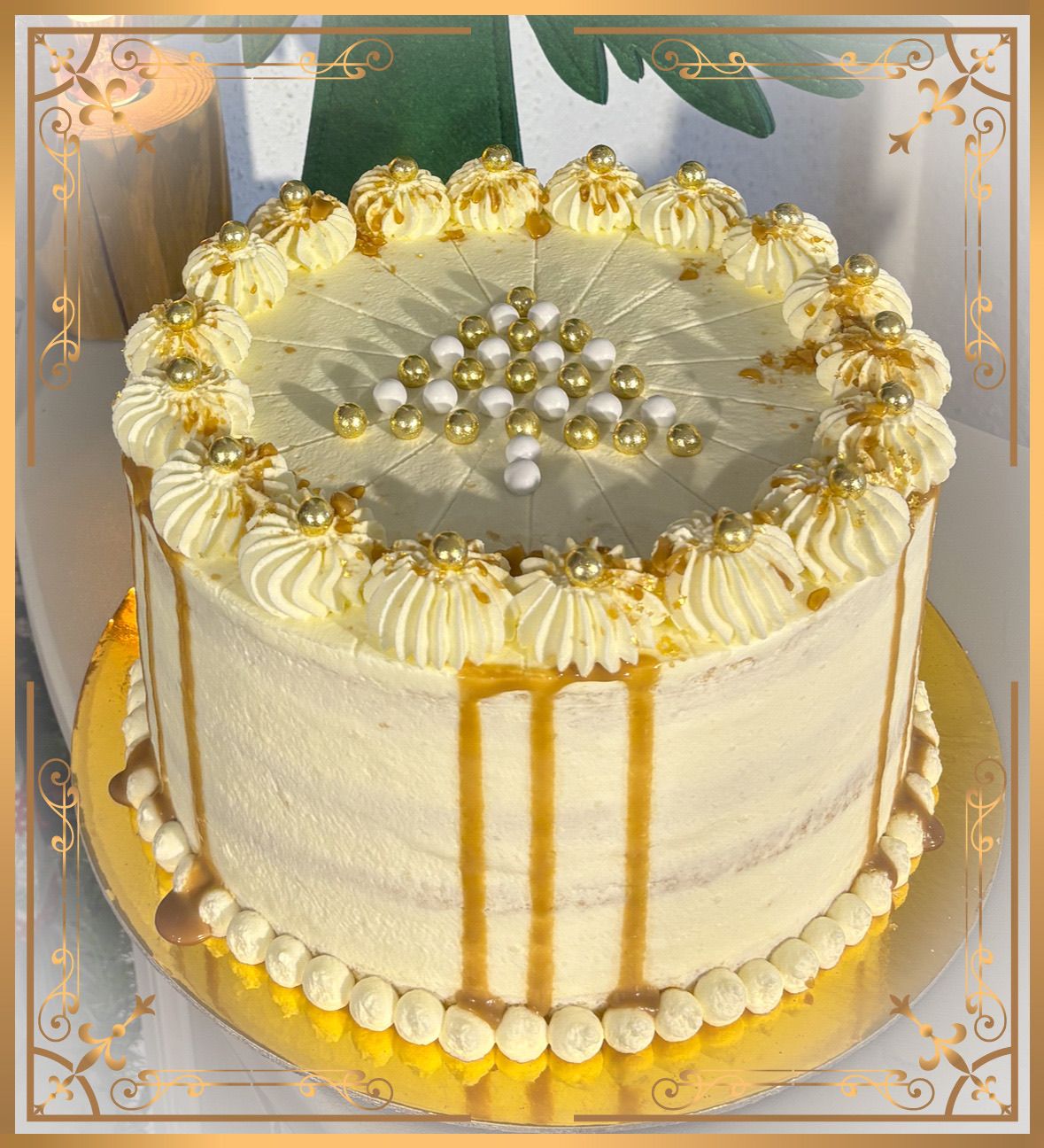 Ein runder Kuchen mit goldenen und weißen Perlen auf der Oberseite, mit gelber Glasur bedeckt und mit Karamell überzogen.